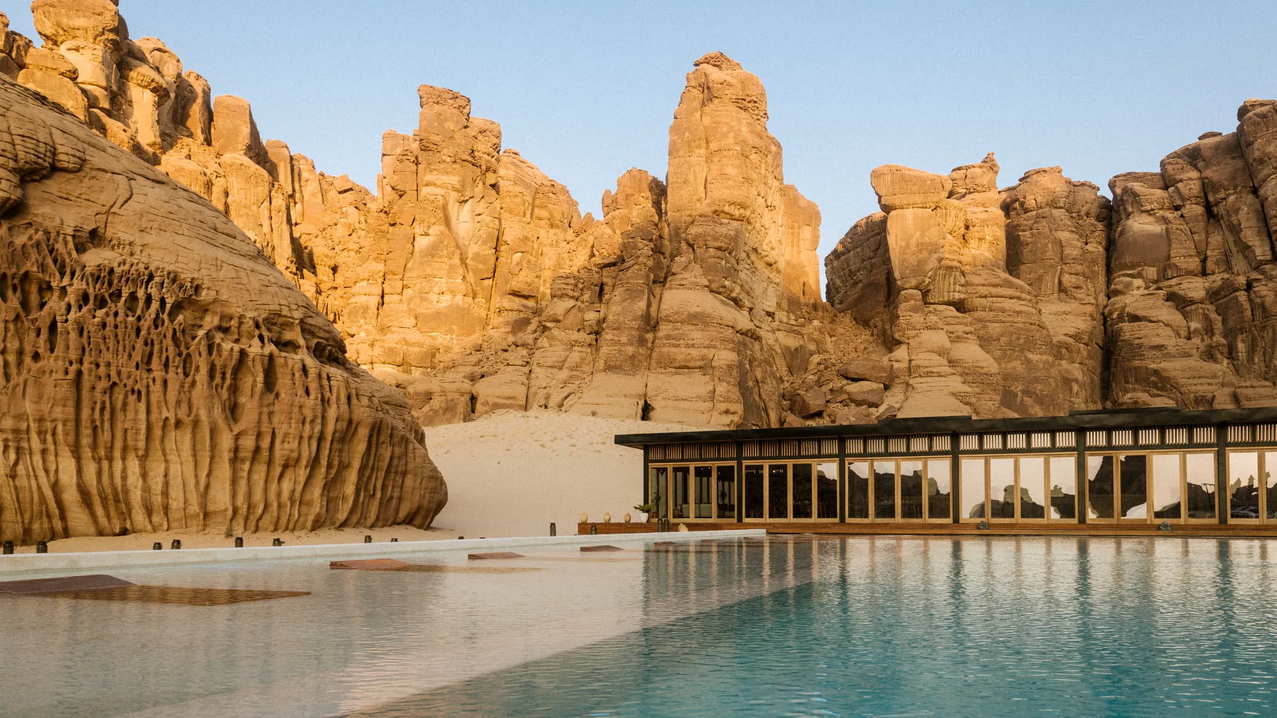 A desert pool set against towering sandstone cliffs at dusk